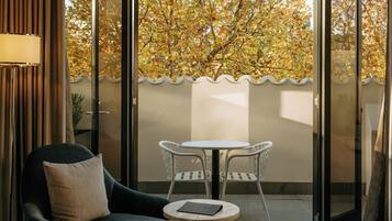 A room with a bed, a chair, a small table, and a view of trees through a glass door.