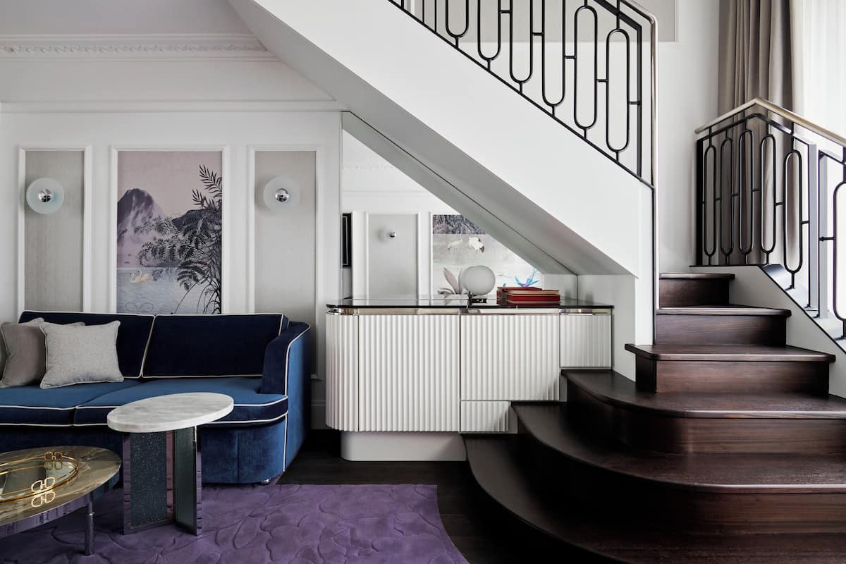 A modern living room with a blue sofa, a small round table, and a staircase with a metal railing.
