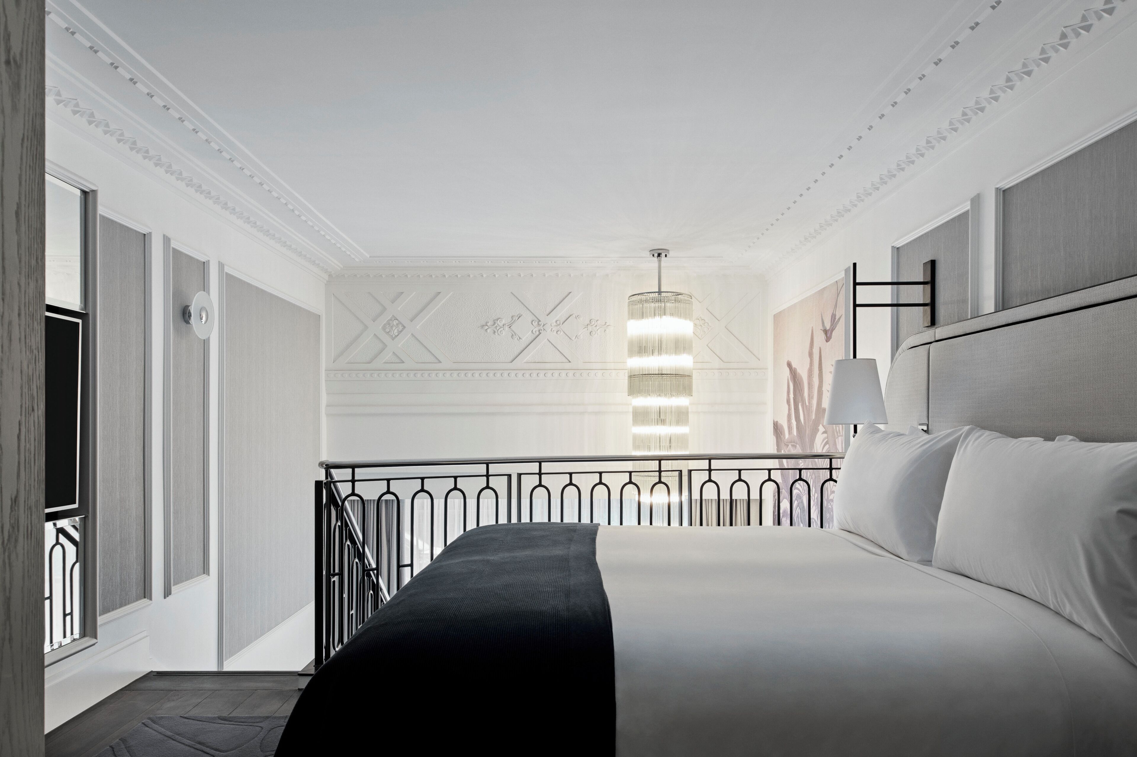 A hotel room with a large bed, a chandelier, a painting, and a view of the outside.