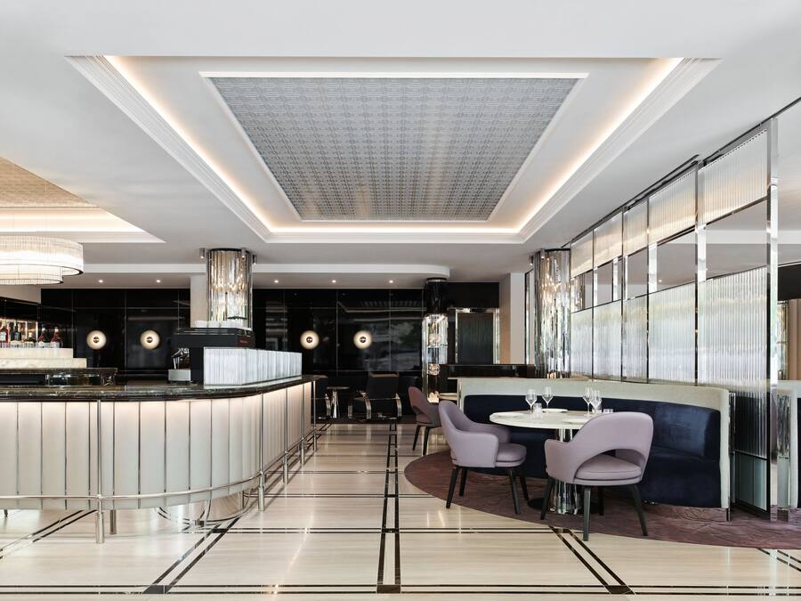 A modern bar area with a curved counter, seating with round tables, and a patterned ceiling.