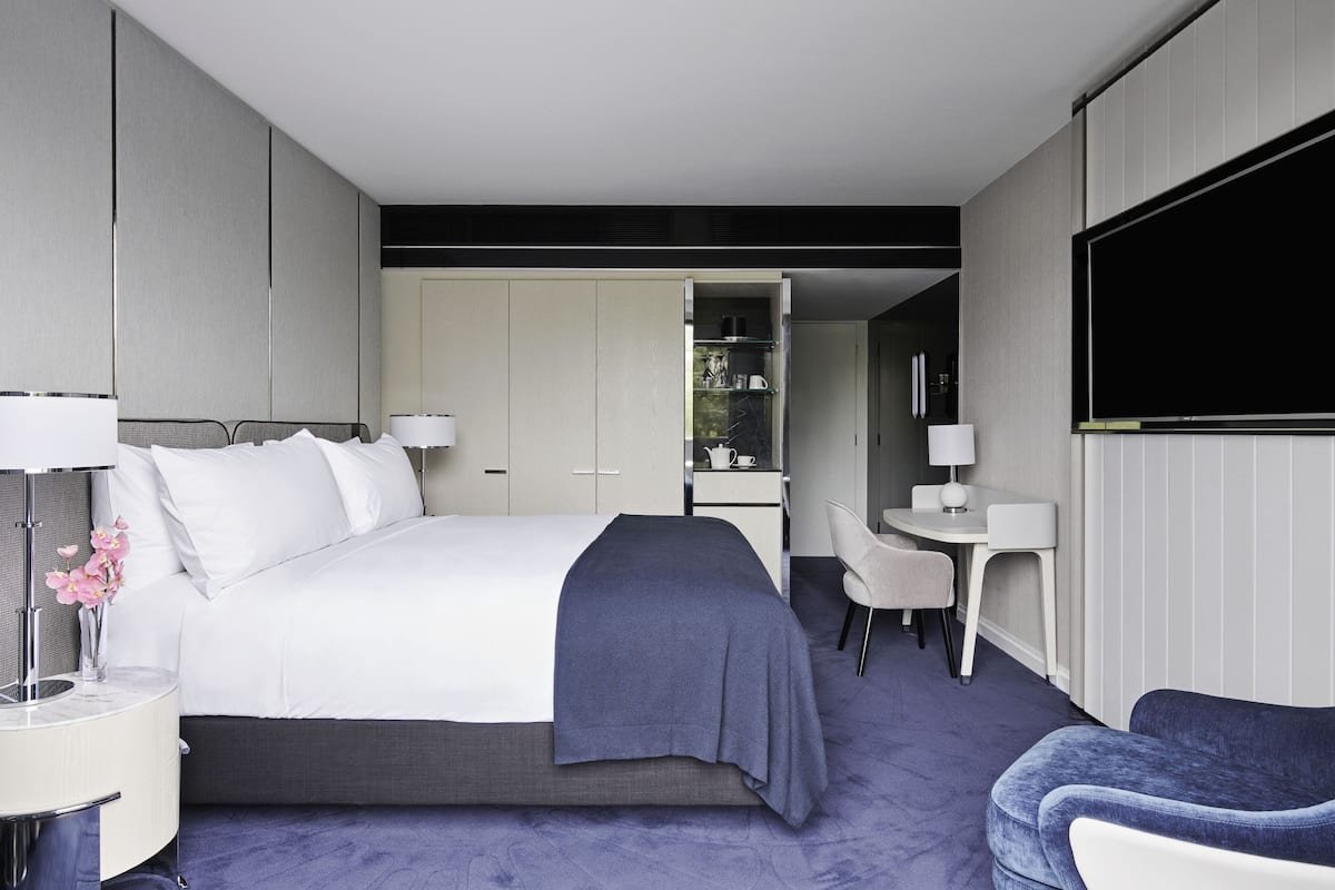 A modern hotel room with a large bed, a desk, a chair, and a TV.