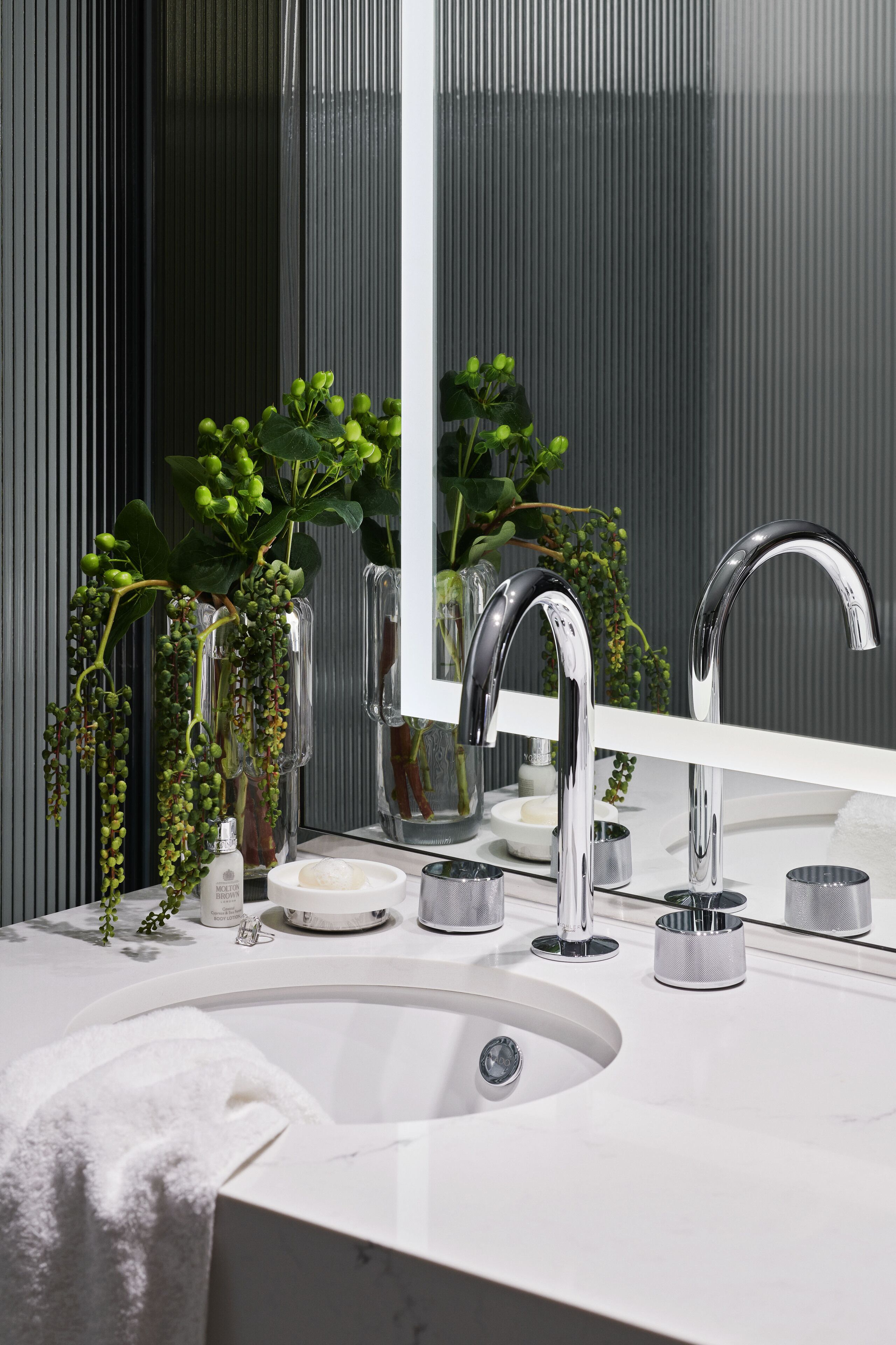 Un baño moderno con un lavamanos blanco, dos grifos cromados y un espejo grande.