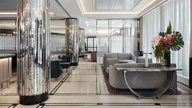 A modern hotel lobby with a central seating area, a reflective column, and a large window with a view. - The Royce (Melbourne)