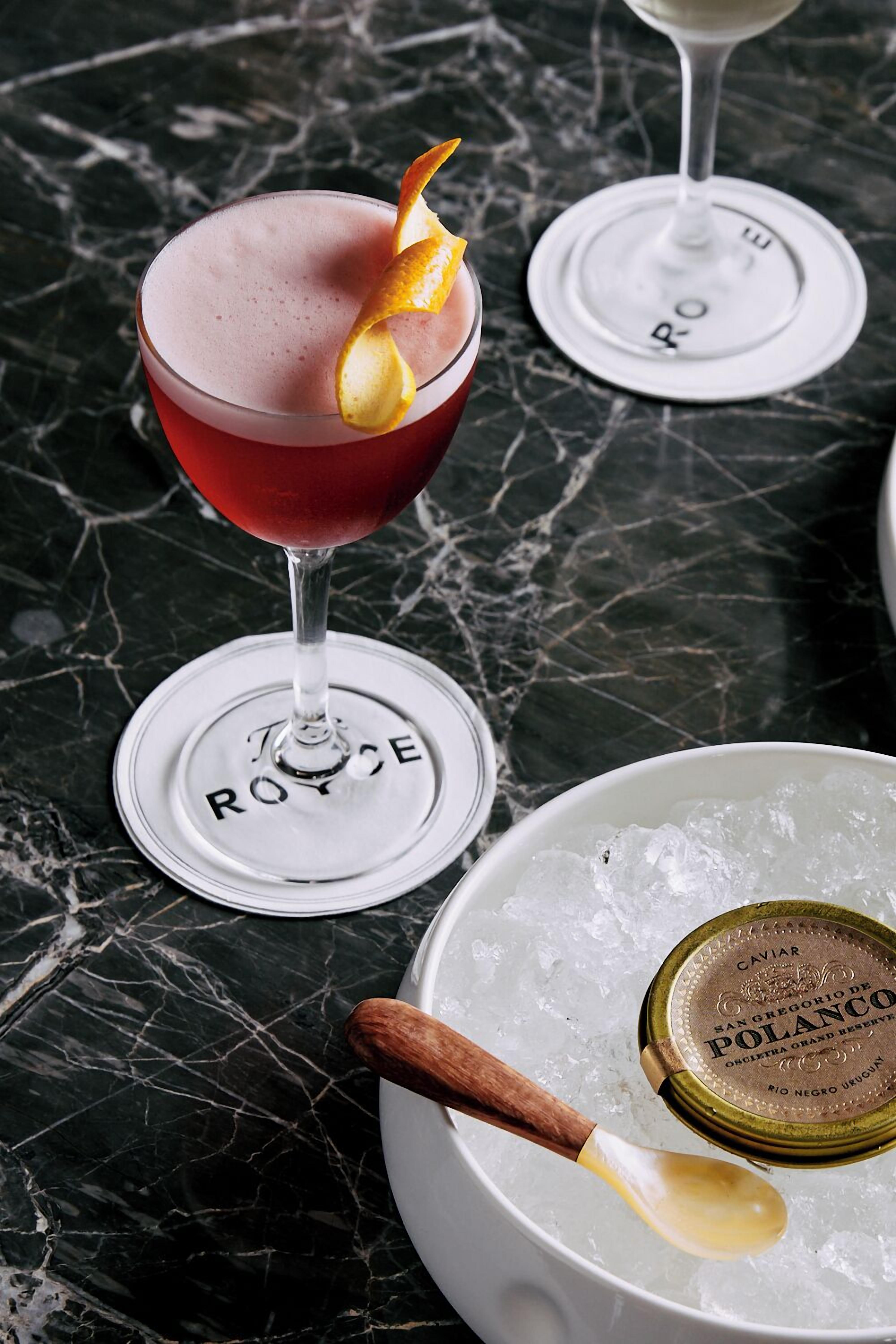 Un verre à martini orné d’une garniture, posé sur une surface en marbre, avec une cuillère et une bouteille de caviar Polanco à proximité.