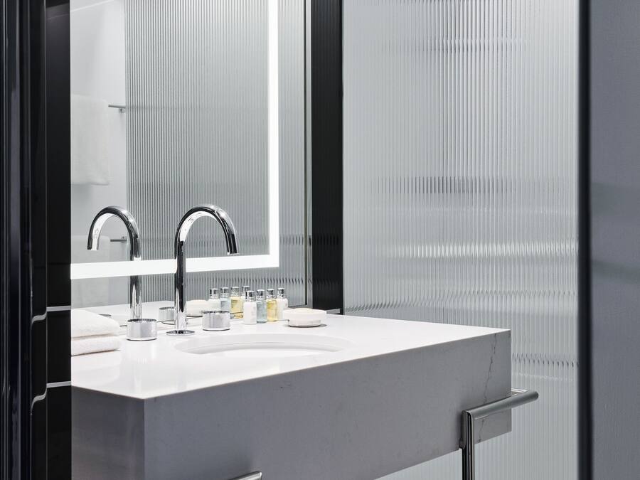 Un baño moderno con un espejo grande, un lavamanos blanco y grifería de cromo.