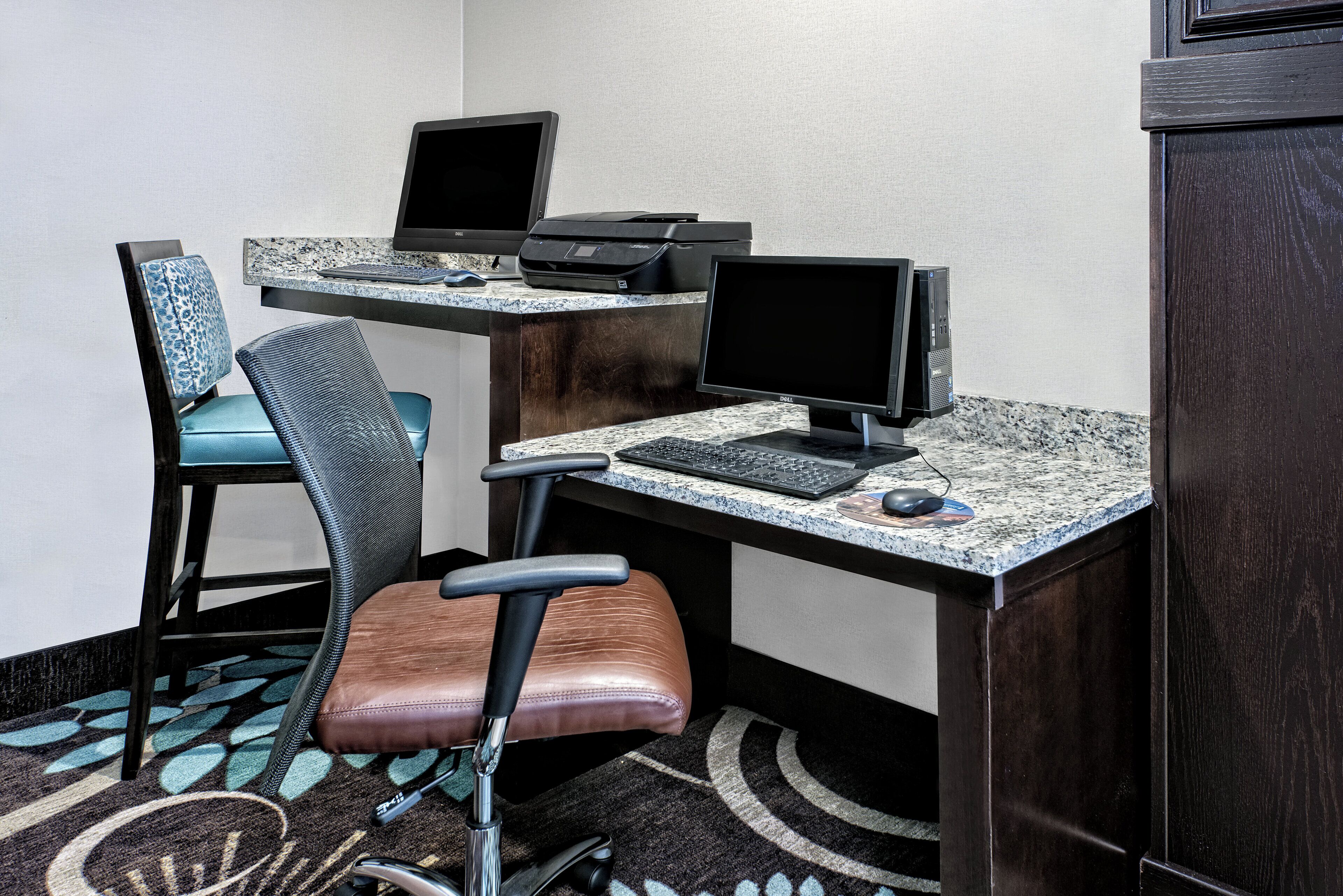 Un espace de travail comprenant deux bureaux, chacun équipé d’un écran d’ordinateur, d’un clavier et d’une souris. On y trouve également deux chaises de bureau, de modèles différents.