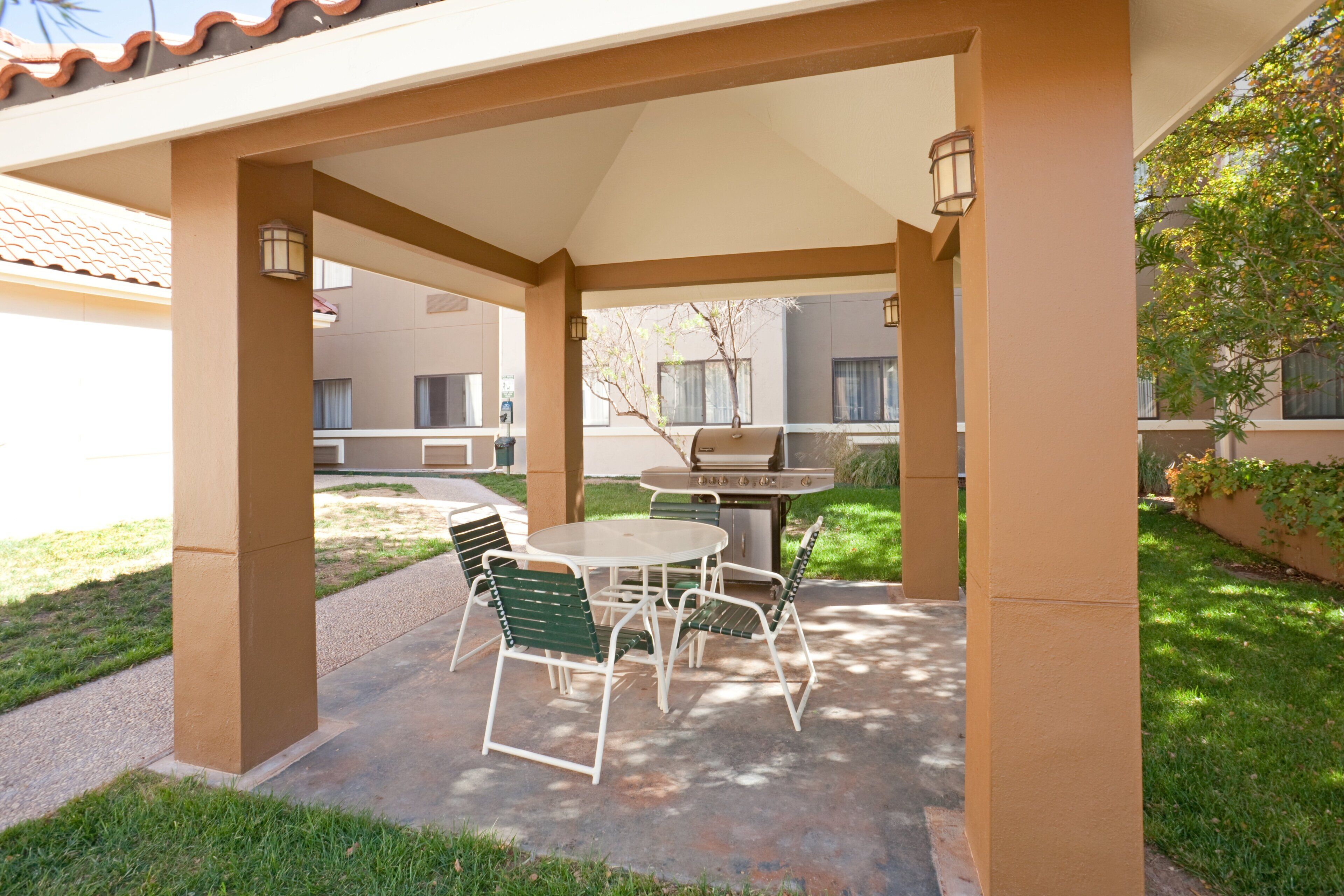 Un patio al aire libre con mesa y sillas, una parrilla y un área techada con columnas.