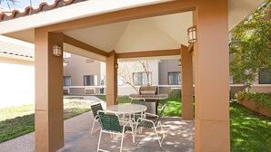 Une terrasse extérieure avec une table et des chaises, un barbecue et un espace abrité avec des colonnes.