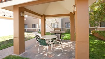 Un patio al aire libre con mesa y sillas, una parrilla y un área techada con columnas.
