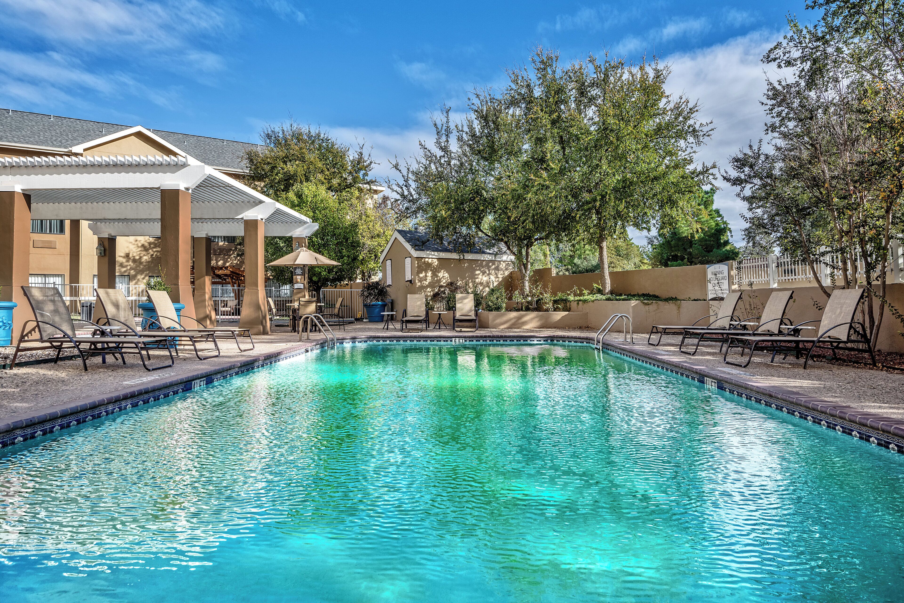 A swimming pool with lounge chairs and a covered seating area.