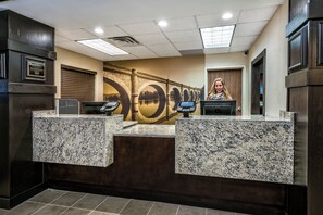 A reception desk with a stone counter, a large wall mural, and a door to the right. - Staybridge Suites Lubbock - University Area by IHG (Lubbock)