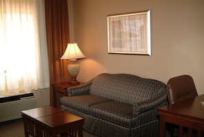 Ein Hotelzimmer mit Sofa, Tisch, Lampe, einem gerahmten Bild an der Wand und einem Fenster mit Vorhängen.