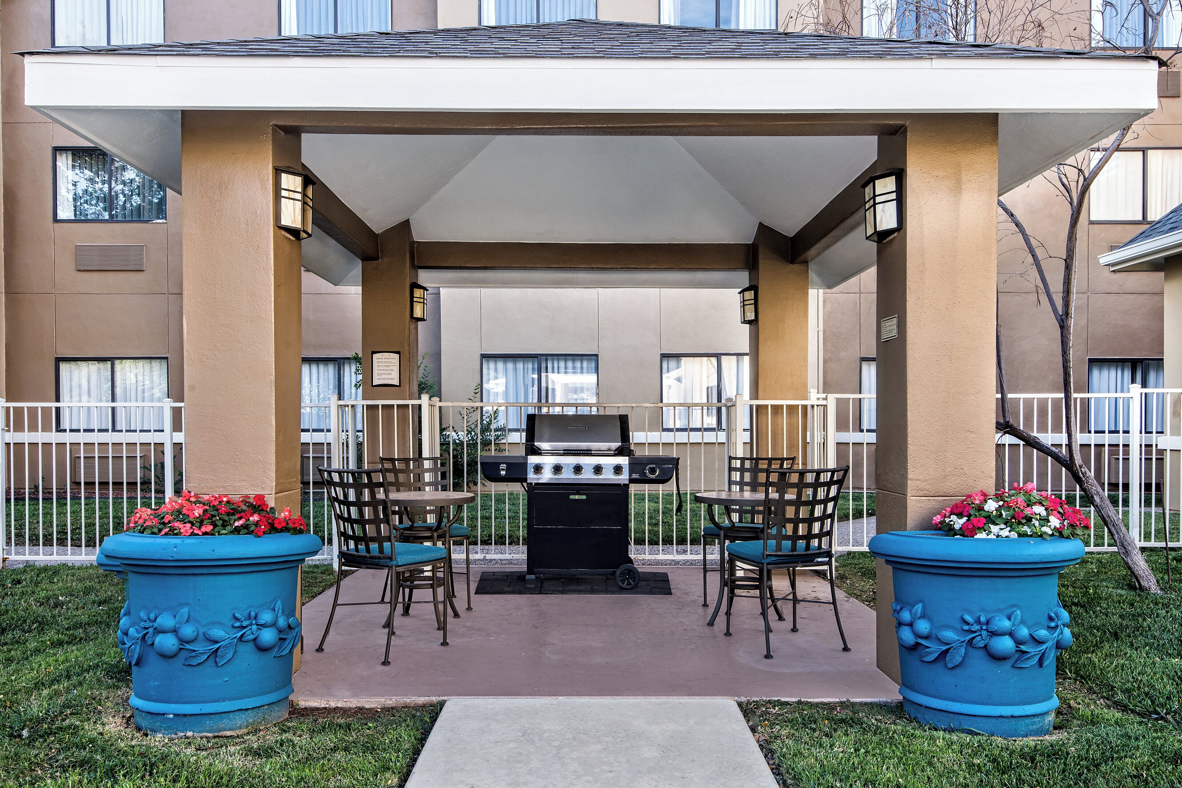An outdoor patio area with a grill, two chairs, and two large flower pots.