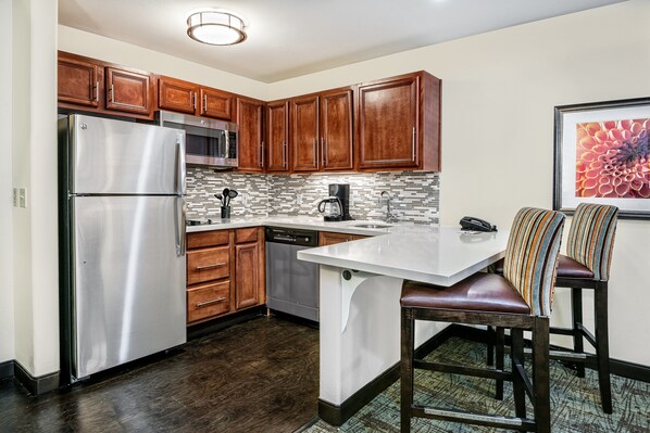 A modern kitchen with wooden cabinets, stainless steel appliances, and a tiled backsplash. - Staybridge Suites Lubbock - University Area by IHG (Lubbock)
