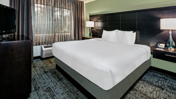 A hotel room with a large bed, a flat-screen TV, a desk, and a lamp. - Staybridge Suites Lubbock - University Area by IHG (Lubbock)