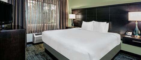 A hotel room with a large bed, a flat-screen TV, a desk, and a lamp.