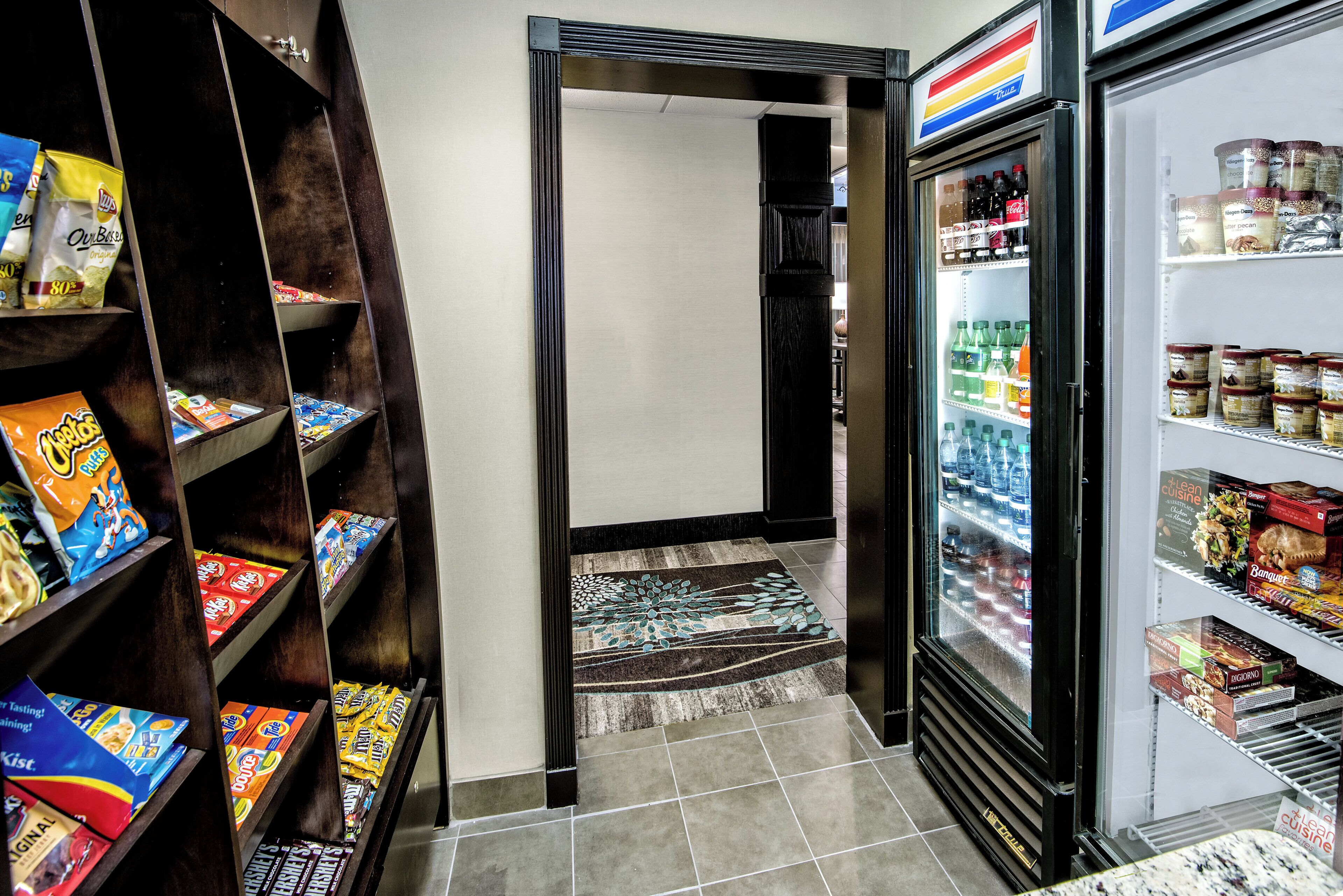 A snack and beverage area with shelves stocked with various snacks and a refrigerator containing bottled water and beverages.