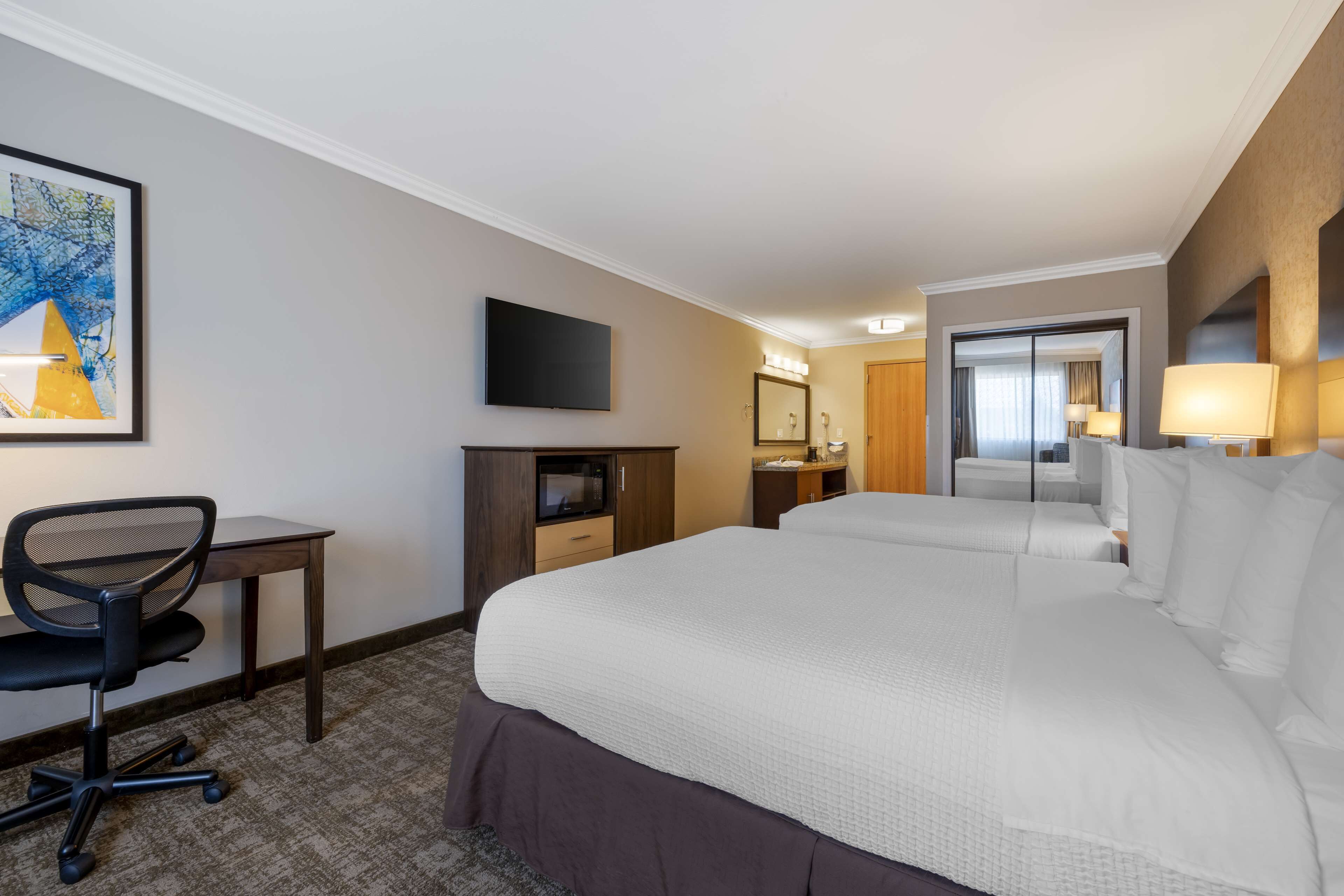 Habitación de hotel con una cama grande, un escritorio con silla, televisión, espejo y una puerta que da a otra habitación.
