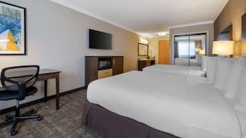 Habitación de hotel con una cama grande, un escritorio con silla, televisión, espejo y una puerta que da a otra habitación.