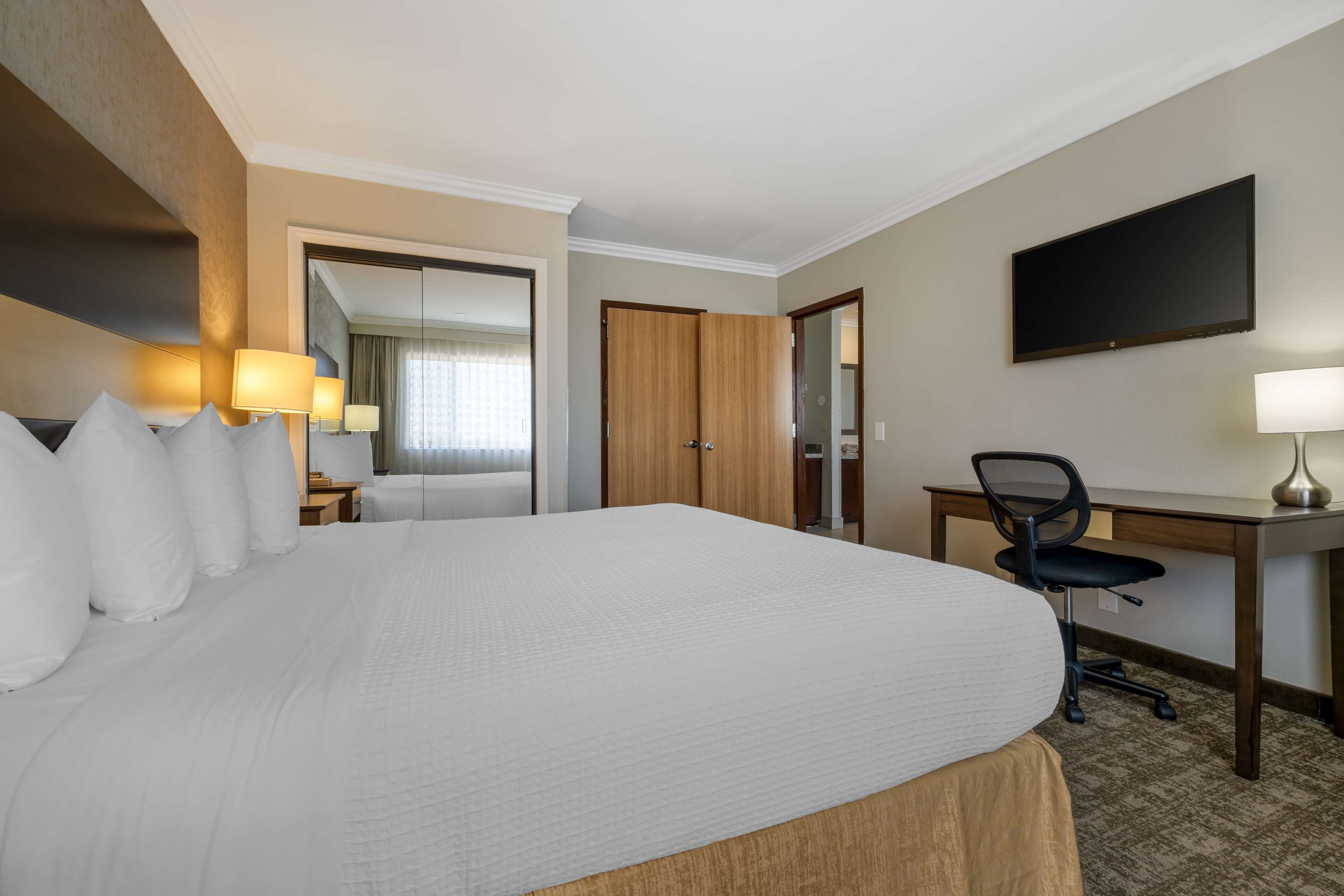 A hotel room with a large bed, a desk, a chair, a flat-screen TV, and a door leading to another room.