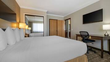 A hotel room with a large bed, a desk, a chair, a flat-screen TV, and a door leading to another room.