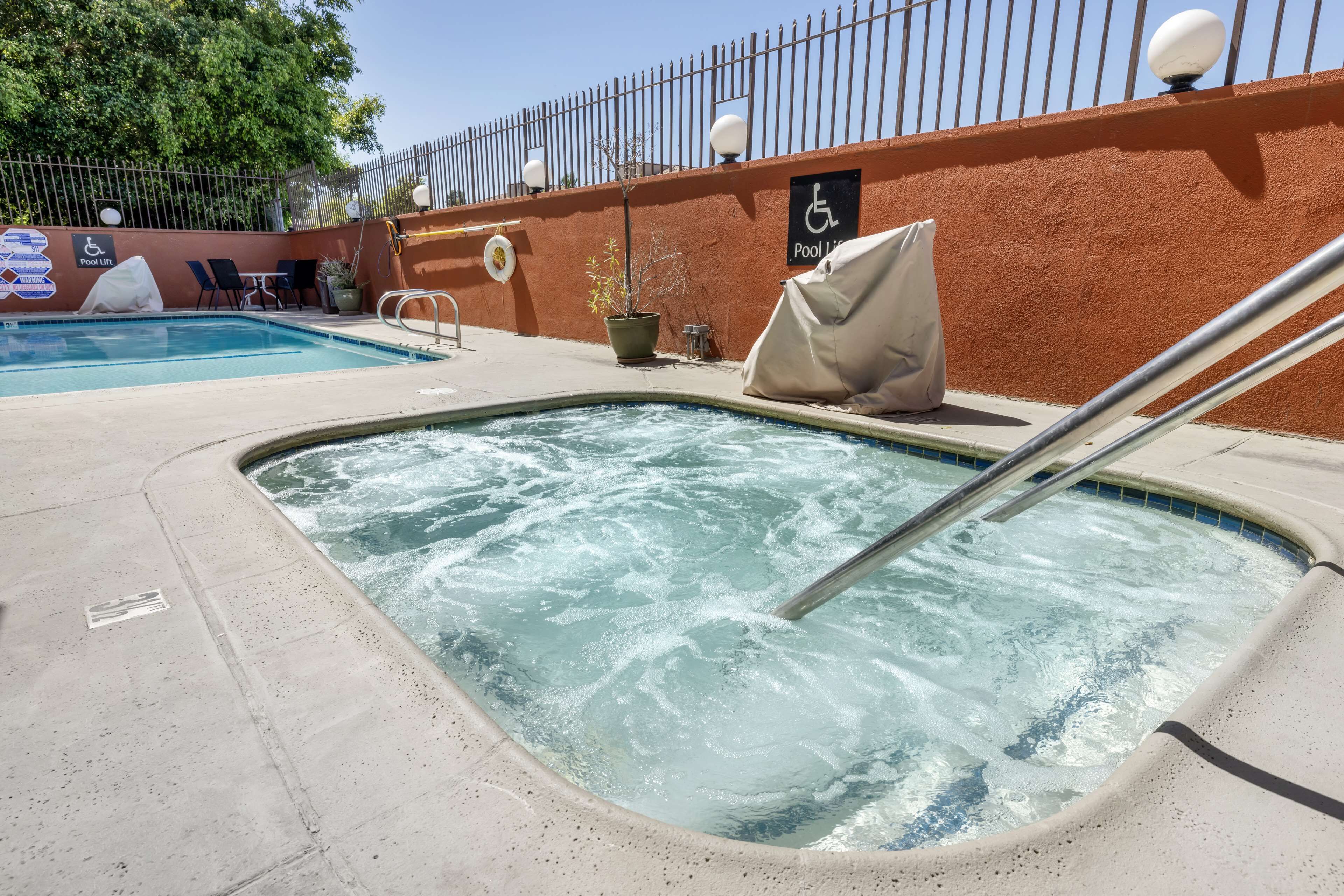 A hot tub area with a pool in the background, a lifeguard chair, and a wheelchair-accessible sign.