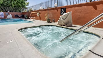 A hot tub area with a pool in the background, a lifeguard chair, and a wheelchair-accessible sign.