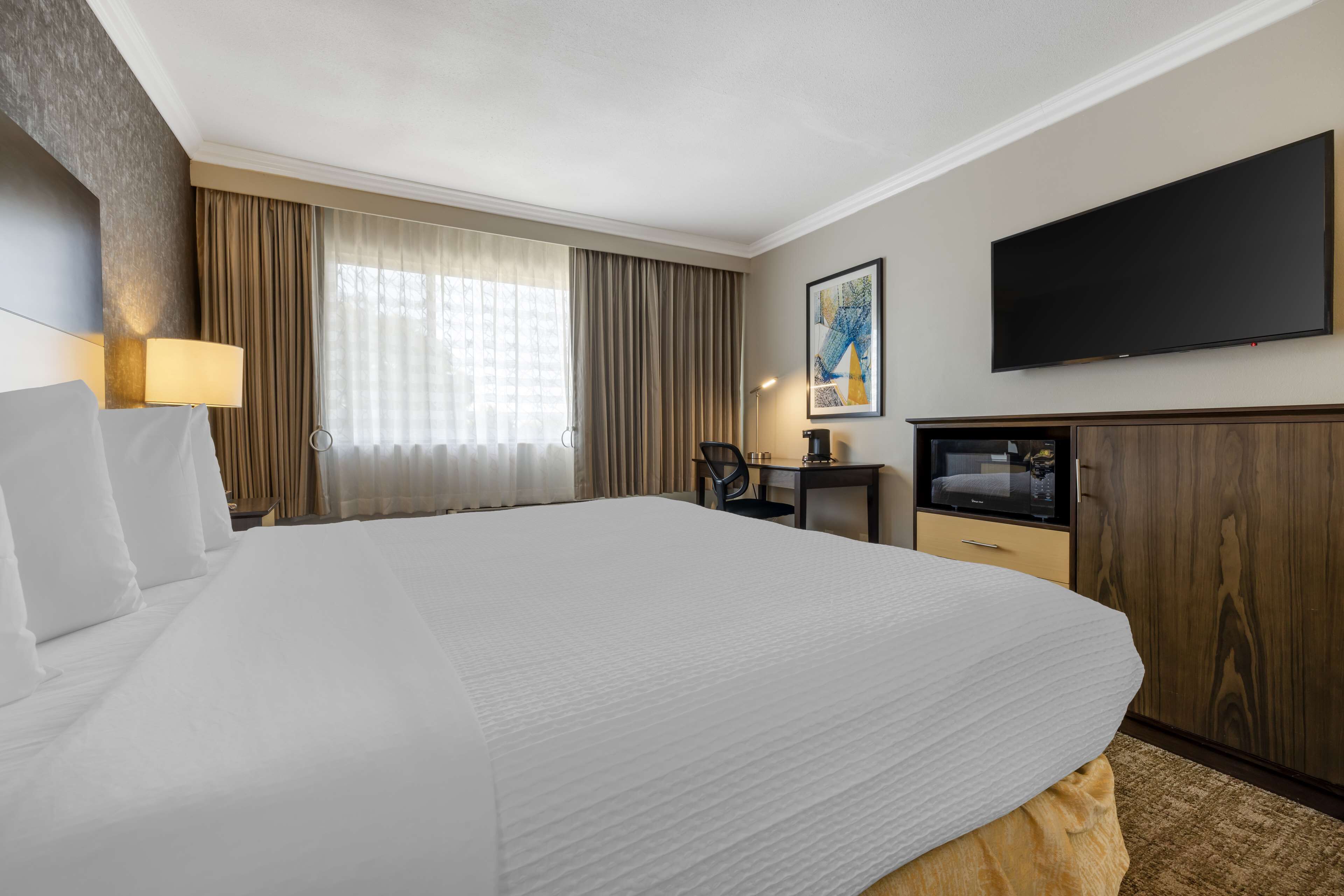 Habitación de hotel con una cama grande, televisión de pantalla plana, escritorio con silla y ventana con cortinas.