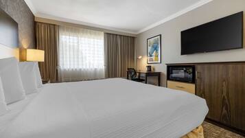 Habitación de hotel con una cama grande, televisión de pantalla plana, escritorio con silla y ventana con cortinas.