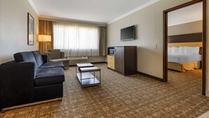 Una habitación de hotel con sofá, televisión, escritorio, cama y ventana con cortinas.