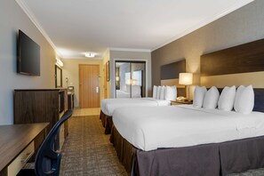 Habitación de hotel con dos camas, un escritorio, una silla, un televisor y una puerta que da a un baño.