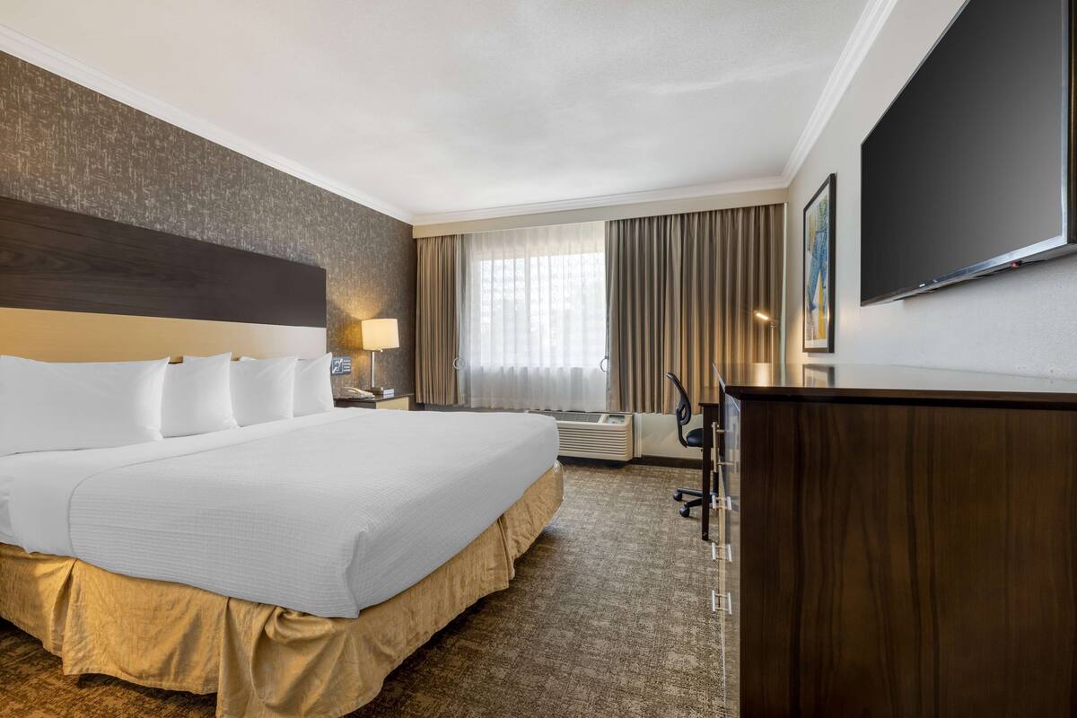 A hotel room with a large bed, a desk, a flat-screen TV, and a window with curtains.