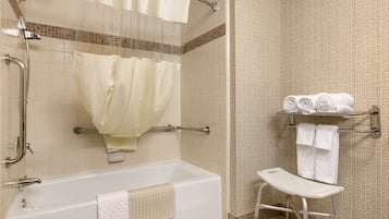 Une salle de bain équipée d’une baignoire, d’une douche avec une porte en verre, d’une barre d’appui, d’une étagère avec des serviettes et d’un banc accessible aux personnes en fauteuil roulant.