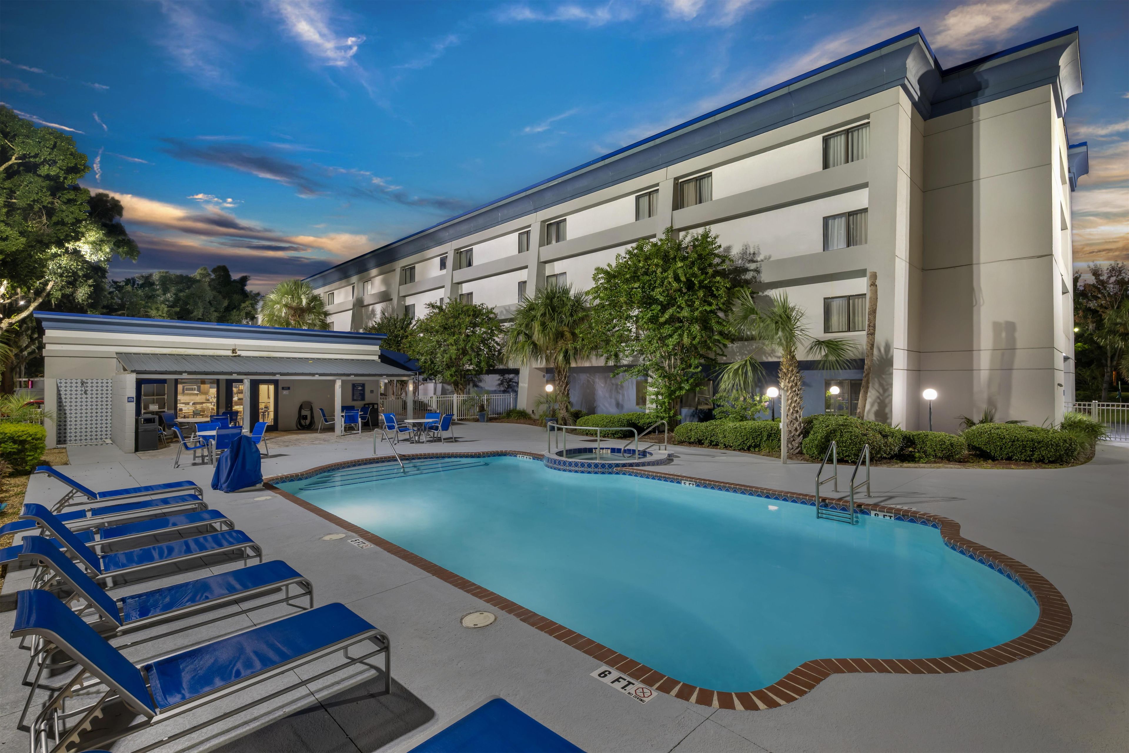 A hotel with a swimming pool, lounge chairs, and a covered area with tables and chairs.