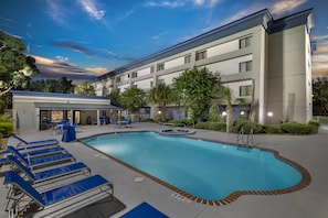 Un hotel con piscina, sillas de descanso y una zona cubierta con mesas y sillas.