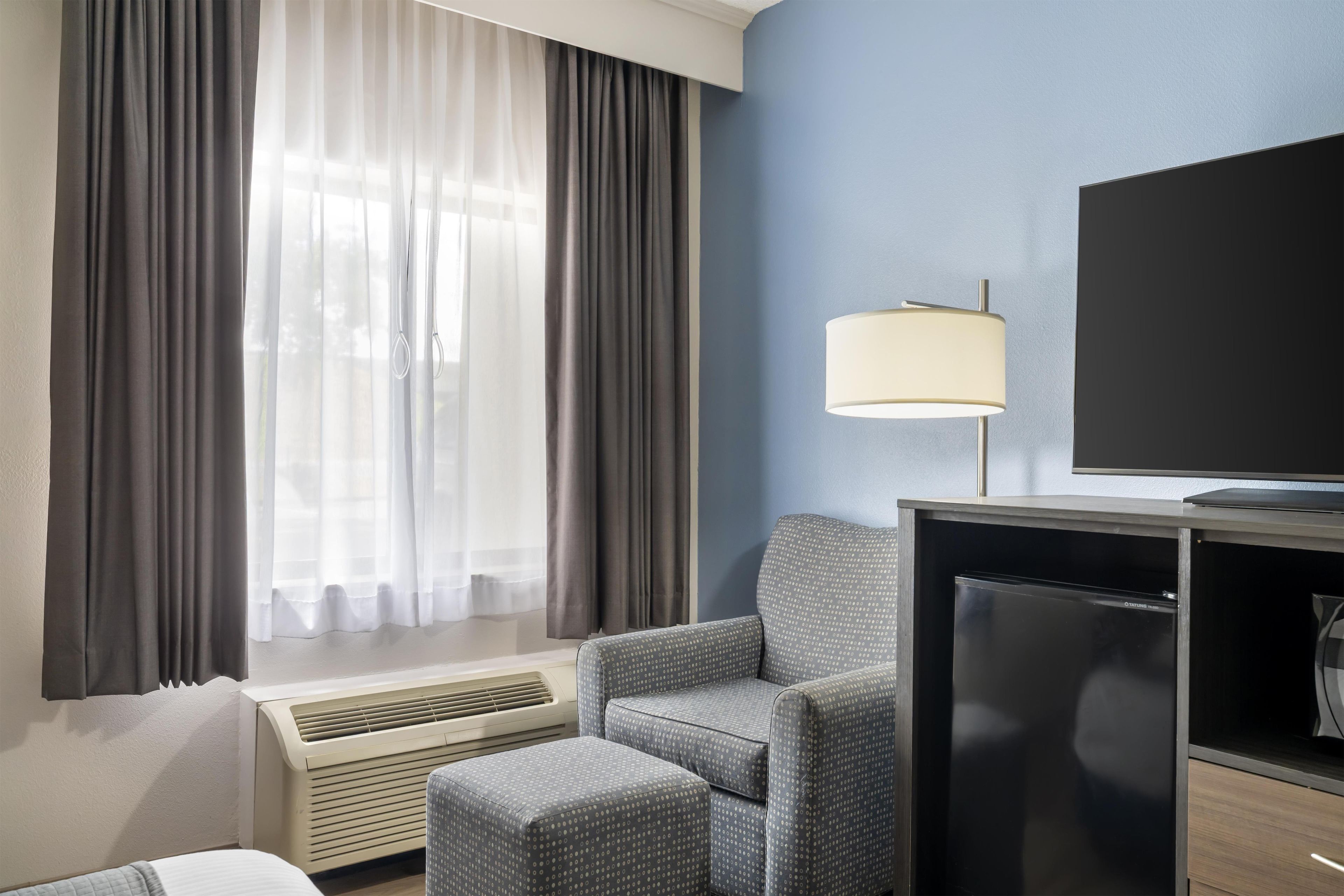 A hotel room with a bed, a chair, a TV, and a heater.