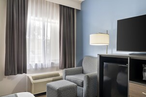 A hotel room with a bed, a chair, a TV, and a heater.