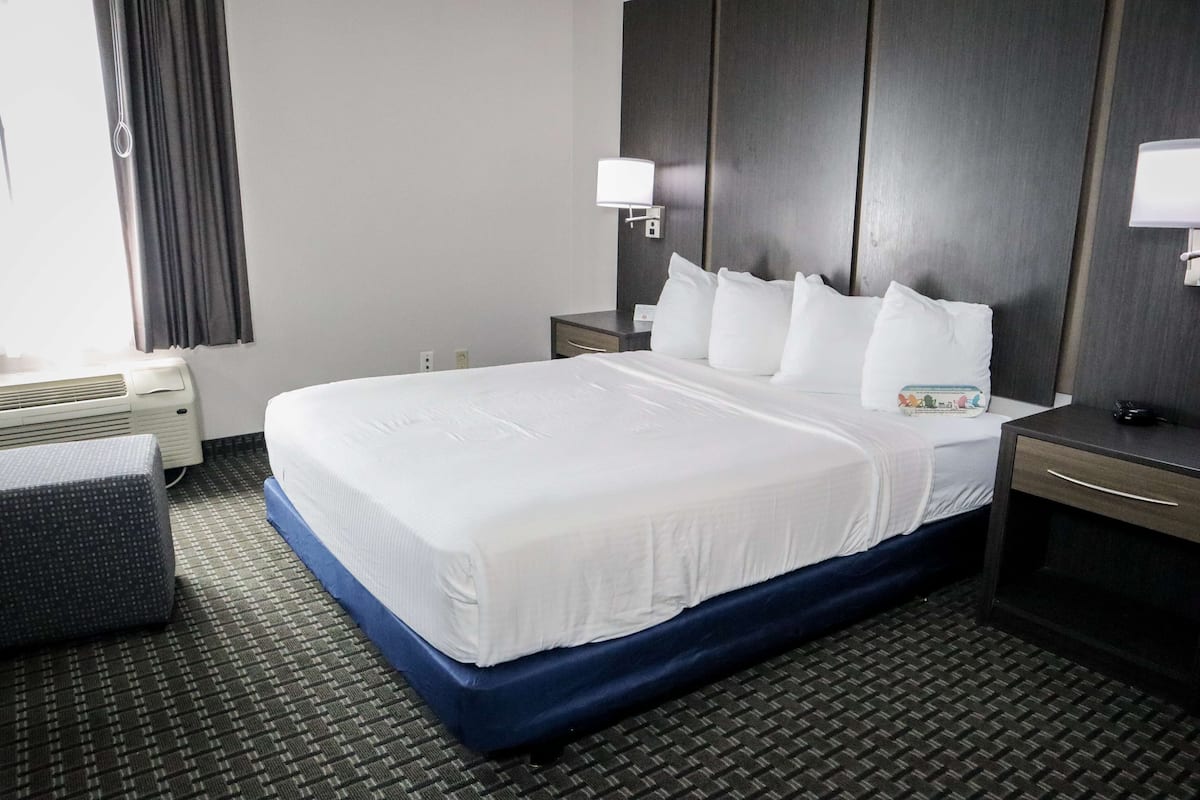 Quarto de hotel com uma cama grande, mesa de cabeceira, abajur, aquecedor e janela com cortinas.