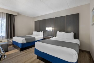 A hotel room with two beds, a desk, a chair, and a window with curtains.