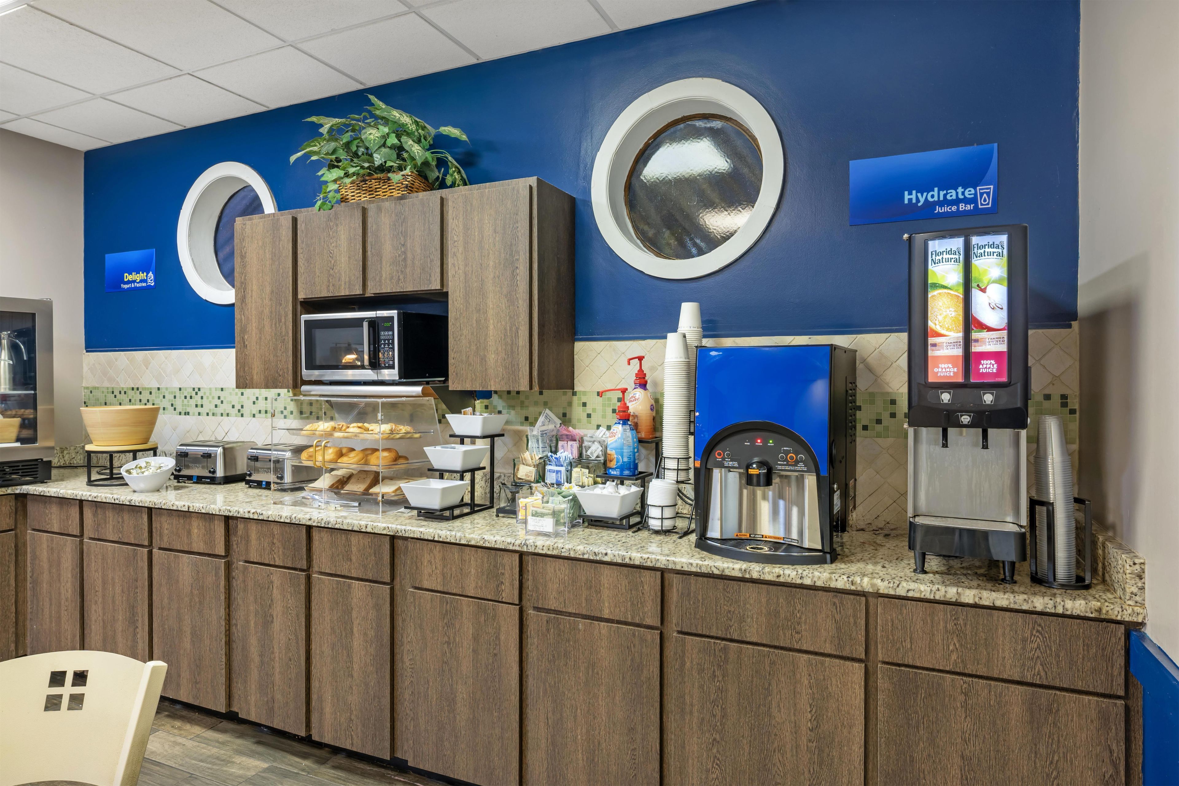 A self-service breakfast area with a coffee machine, juice dispenser, and a microwave.