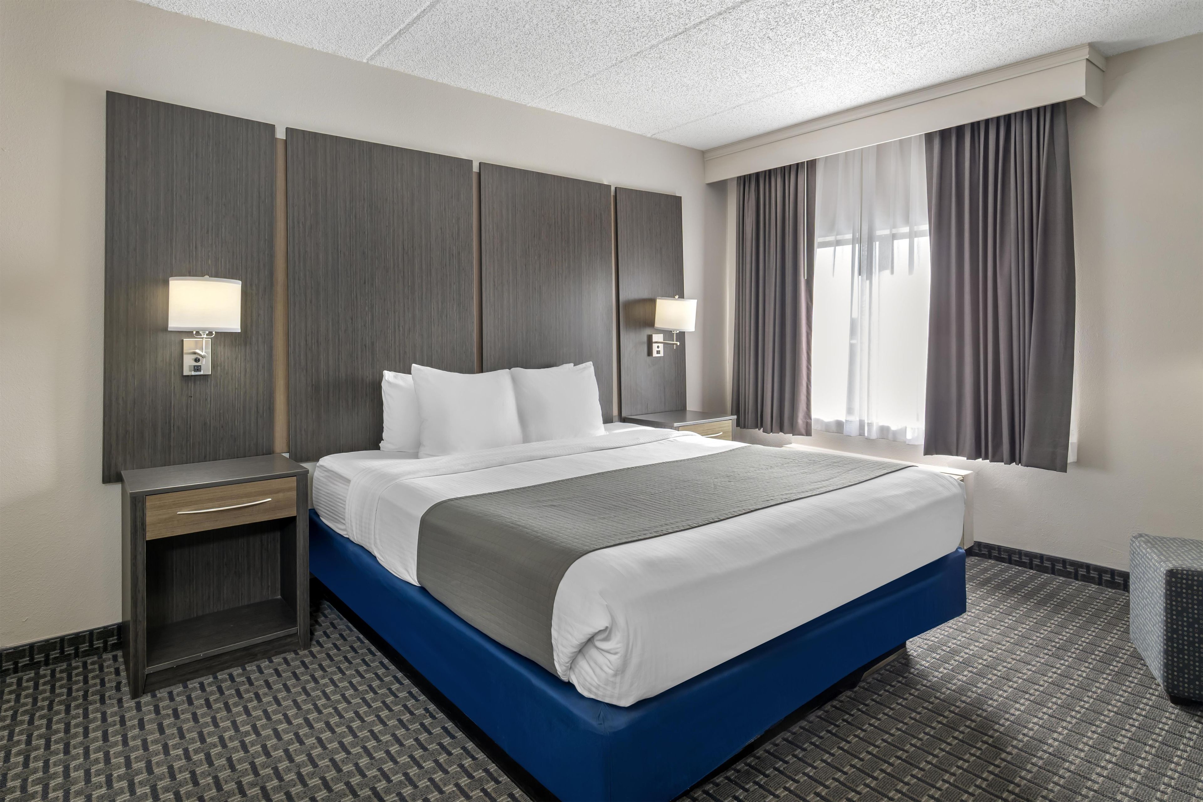 A hotel room with a large bed, bedside lamps, a nightstand, and a window with curtains.