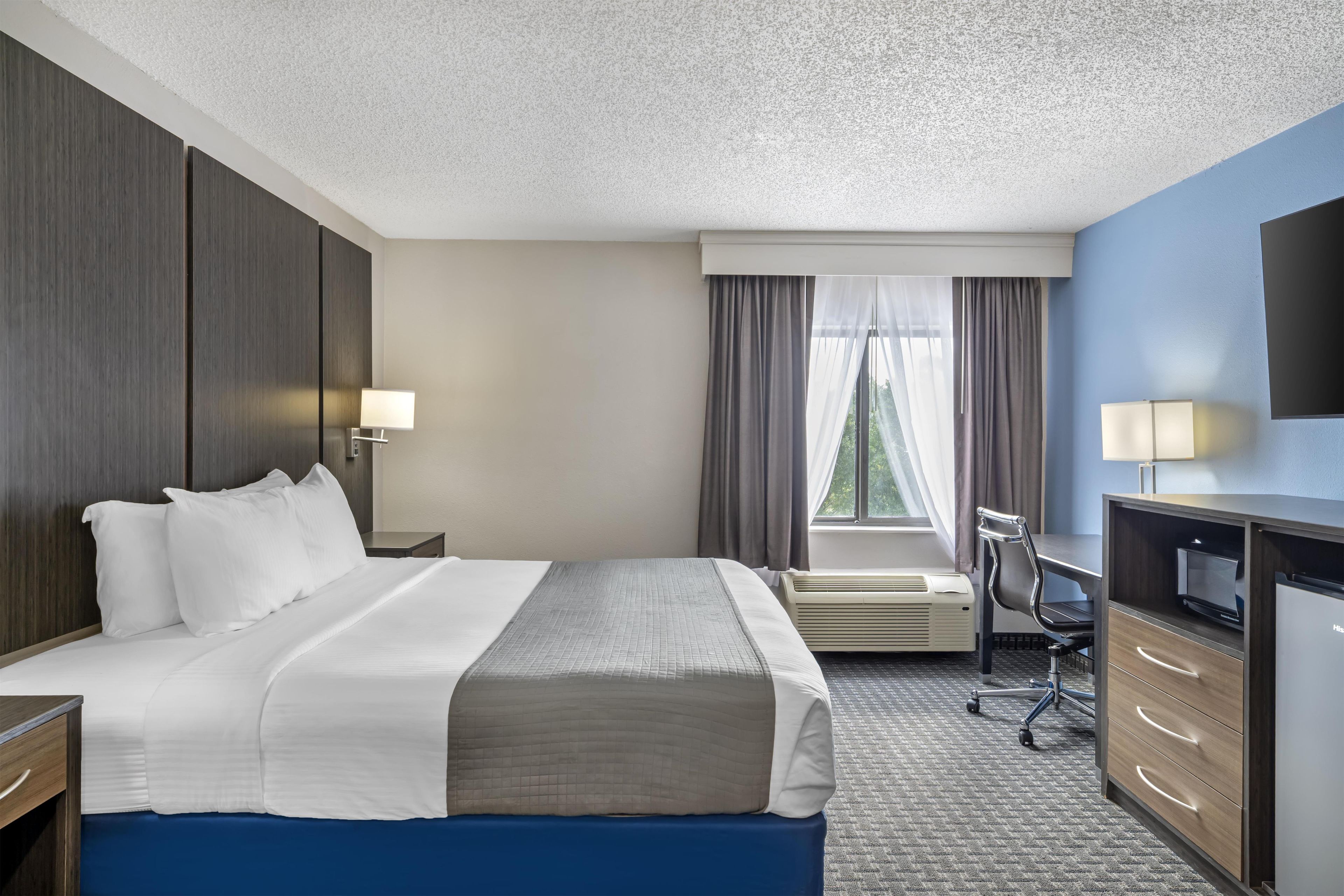 A hotel room with a bed, desk, chair, and a television.