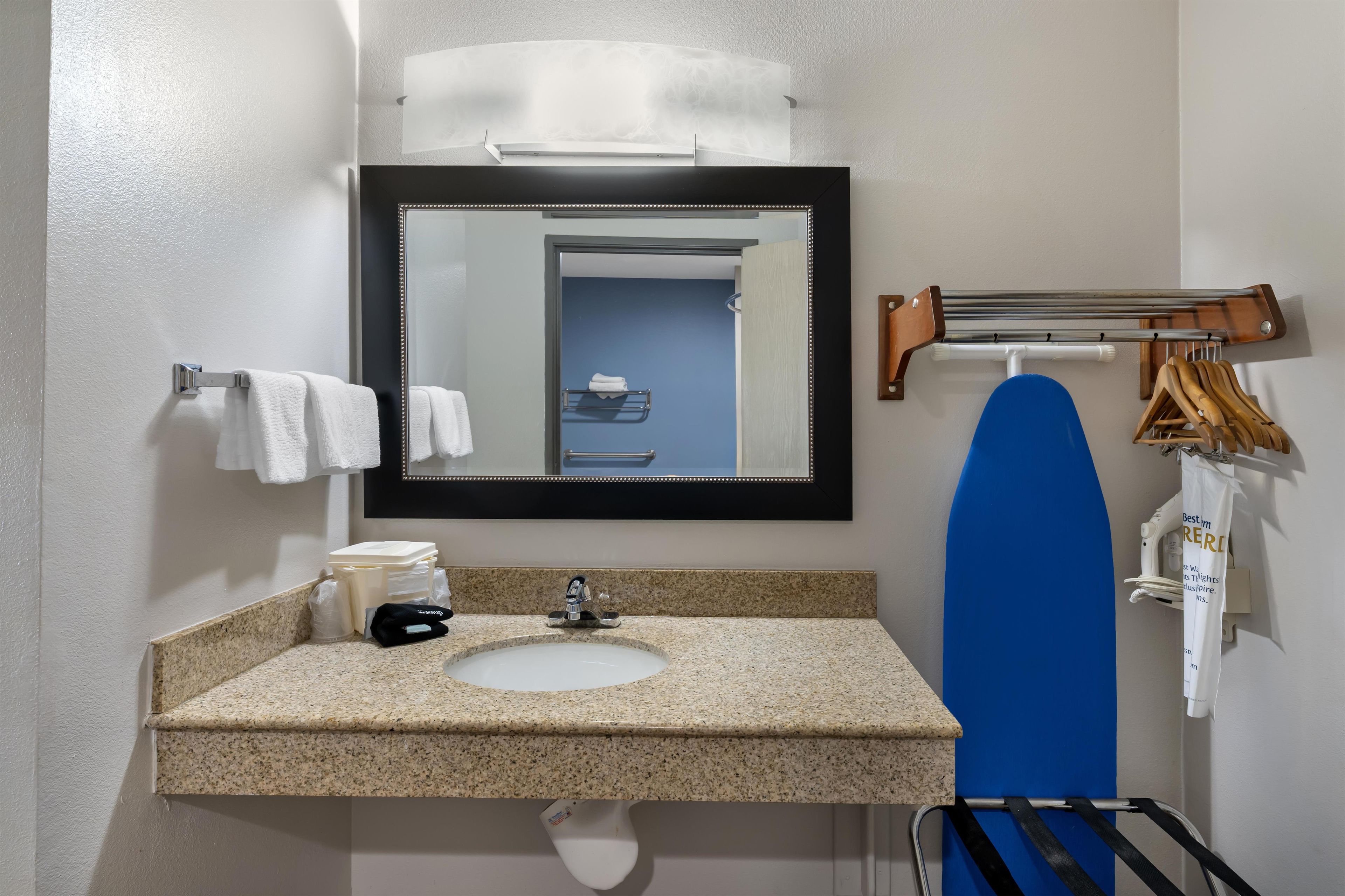A bathroom with a granite countertop sink, a mirror with a wooden frame, and a towel rack.