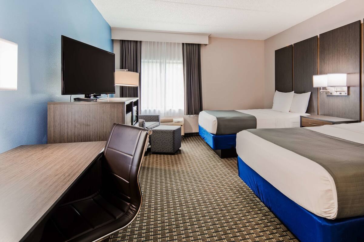 Quarto de hotel com cama grande, escrivaninha, cadeira, televisão e janela com cortinas.