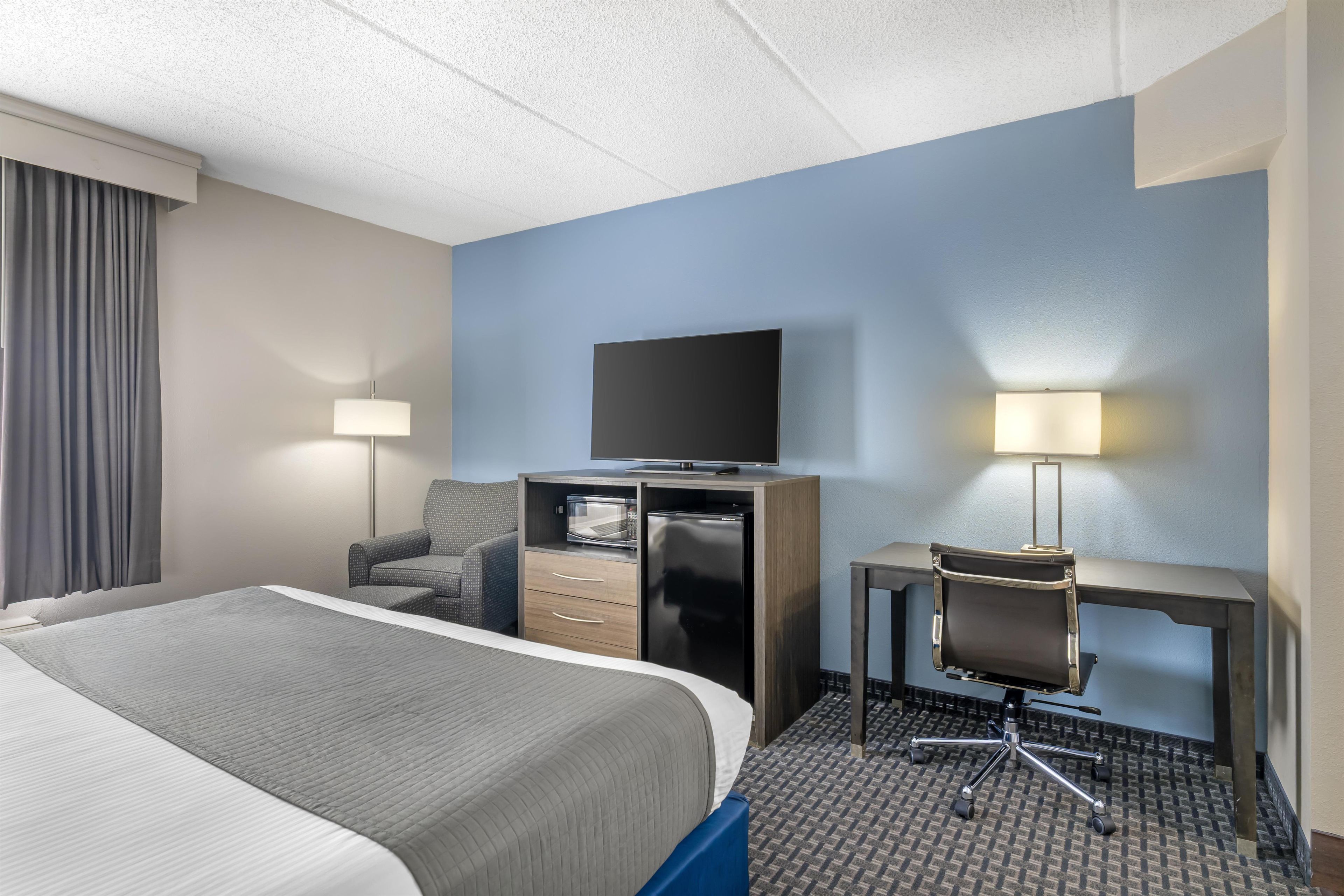 A hotel room with a bed, a desk, a chair, a television, and a microwave.