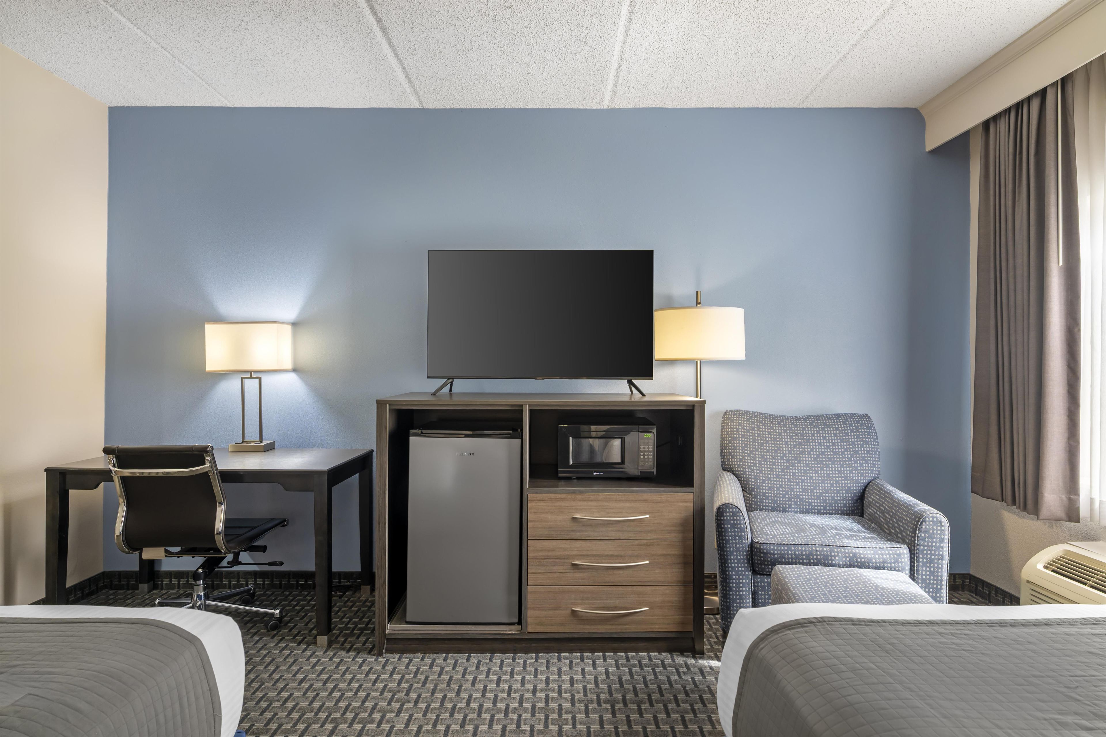 A hotel room with a bed, a desk, a chair, a television, a refrigerator, and a microwave.