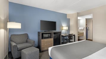 A hotel room with a bed, a desk with a flat-screen TV, a chair, a microwave, and a lamp.