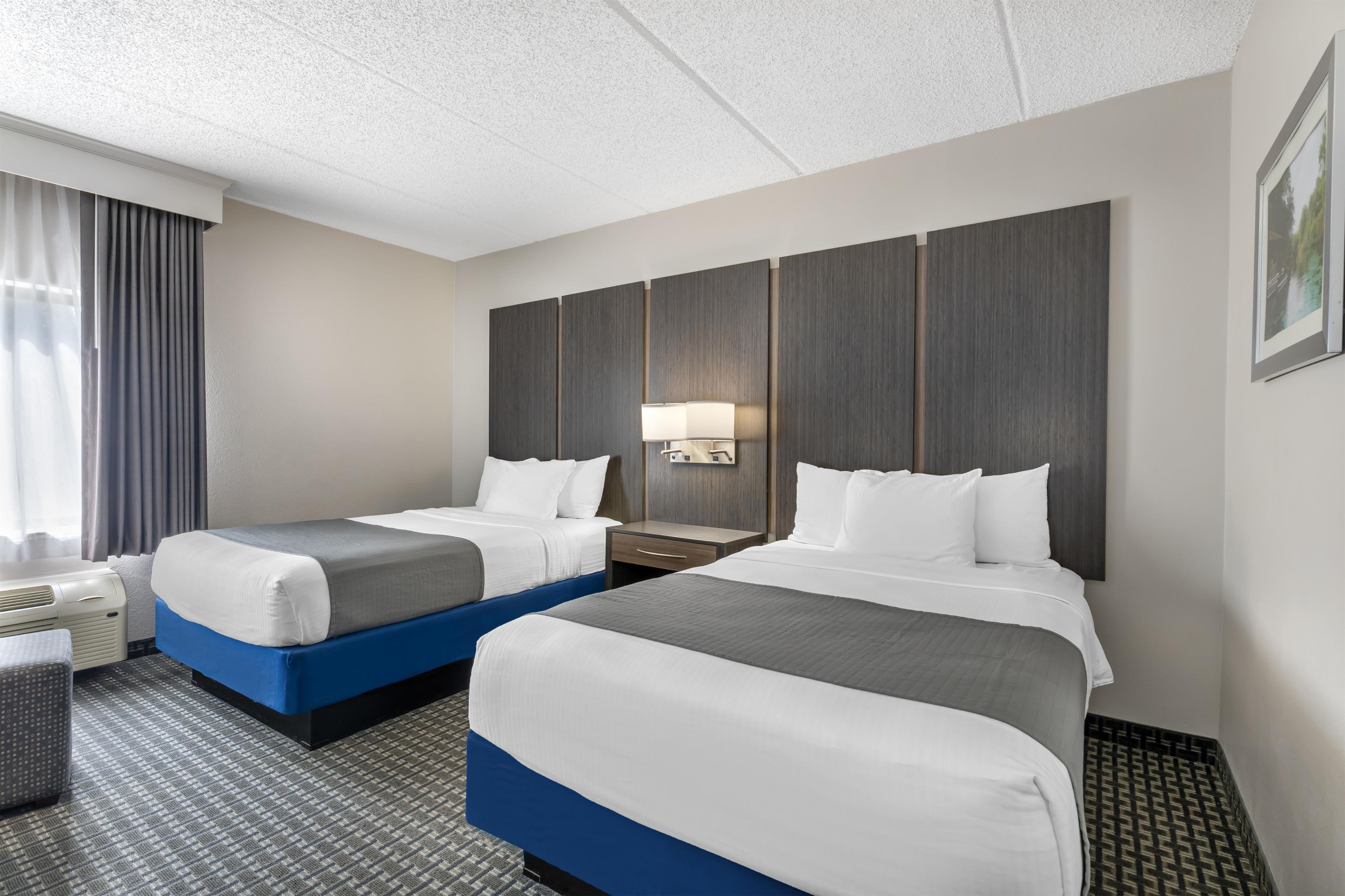 A hotel room with two beds, a desk, a chair, and a large window with curtains.