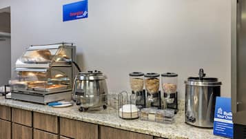 A breakfast buffet setup with a self-service yogurt station, cereal dispensers, and a hot food station.