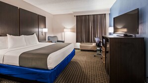Ein Hotelzimmer mit einem großen Bett, einem Schreibtisch mit Stuhl, einem Fernseher und einem Kleiderschrank.